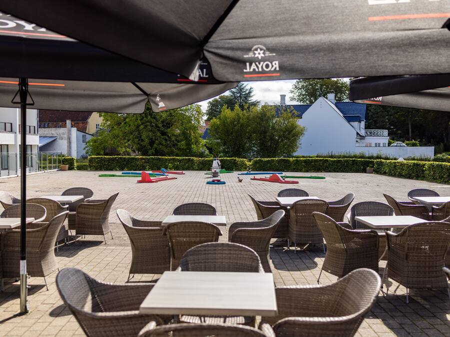 An outdoor seating area with wicker chairs and tables, umbrellas, and a view of buildings and trees in the background.