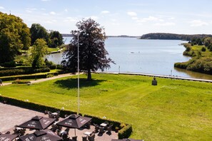 A riverside view with a lawn, seating area, and a large tree. - Milling Hotel Søpark (Maribo)