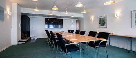 Un salón de conferencias con una larga mesa, sillas e iluminación colgante.