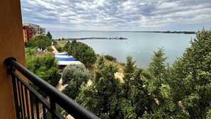 A balcony with a view of a body of water, a distant island, and surrounding greenery. - Menada Ravda Apartments (Pomorie)