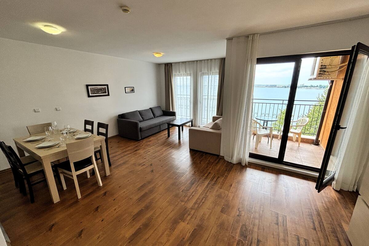 A modern living room with a dining area, a sofa, and a balcony with a view of the sea.