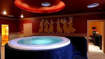Relax in a serene spa room with a large hot tub and a unique ceiling design, surrounded by a beautiful mural and a vase of fresh flowers.