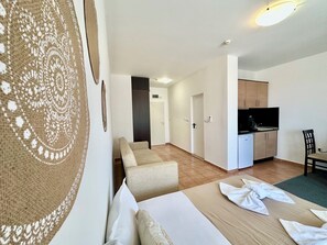 A hotel room with a bed, a sofa, a dining table, and a kitchenette. - Menada Ravda Apartments (Pomorie)