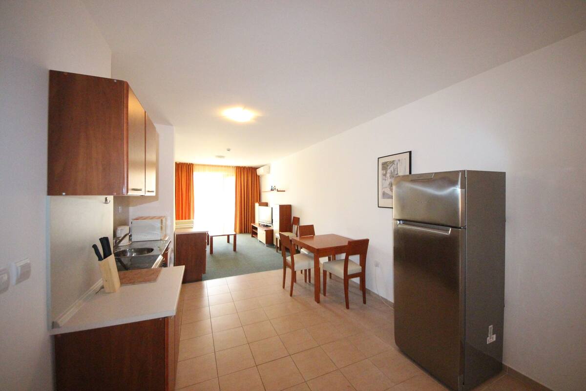 A compact kitchen with a refrigerator, a dining table, and a small seating area.