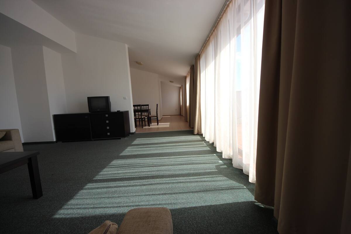 A spacious living room with a large window, a television, a sofa, and a dining area.