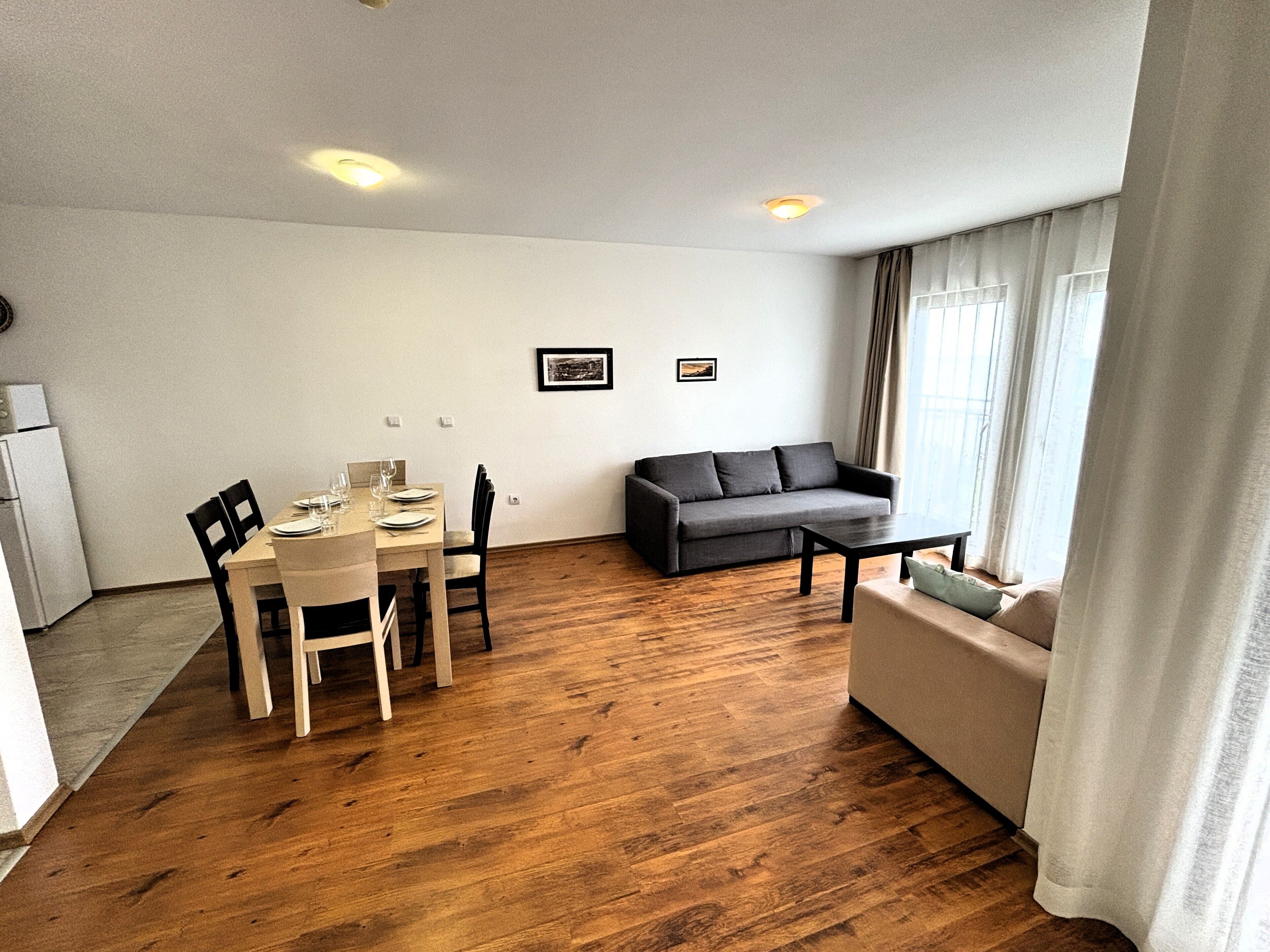 Una sala de estar moderna con comedor, piso de madera, un sofá gris y una pequeña mesa.