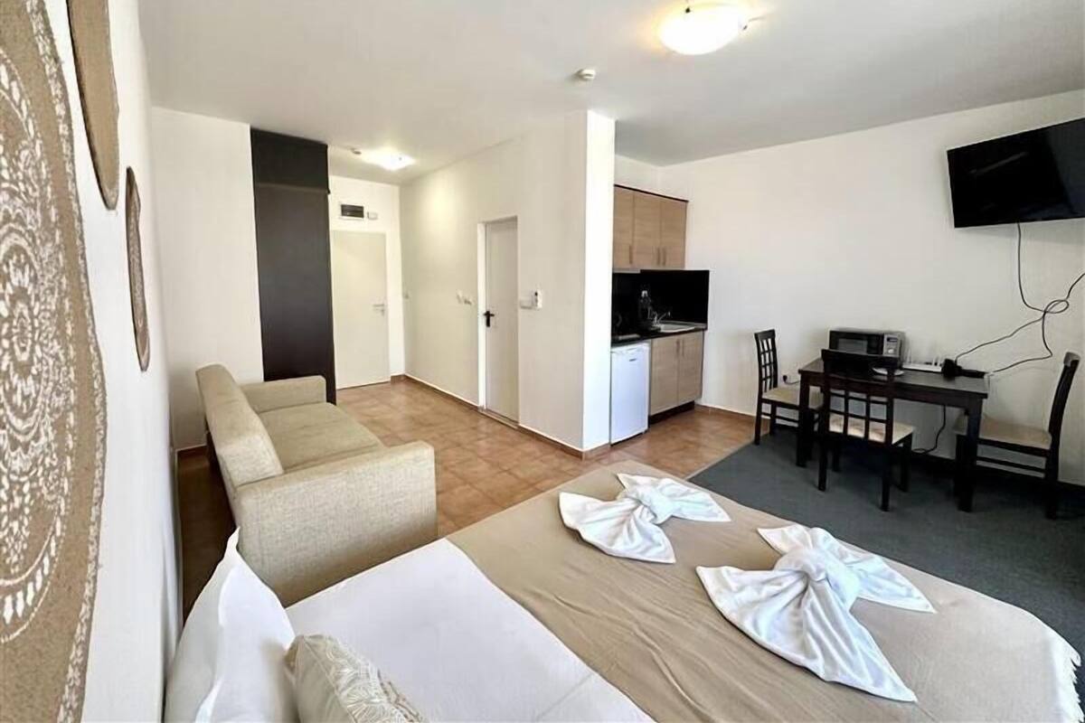 A hotel room with a bed, a desk, a chair, a kitchenette, and a TV.