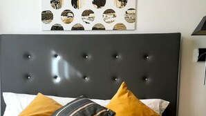 Ein ordentlich bezogenes Bett mit einer gemusterten Tagesdecke, ein aufgerolltes weißes Handtuch und zwei Kissen in Senfgelb und Streifen.