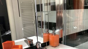 Ein modernes Badezimmer mit einem weißen Waschbecken, einem chromfarbenen Wasserhahn und orangefarbenen Seifenspendern.
