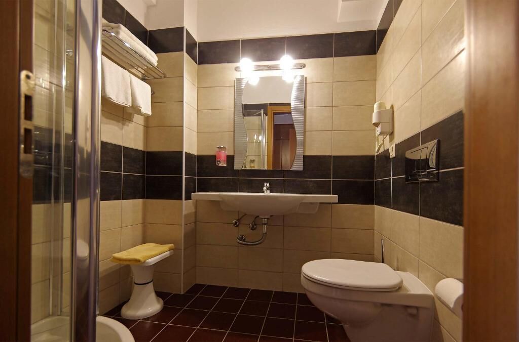 A bathroom with a glass shower enclosure, a white toilet, a sink with a mirror above it, and a towel rack.