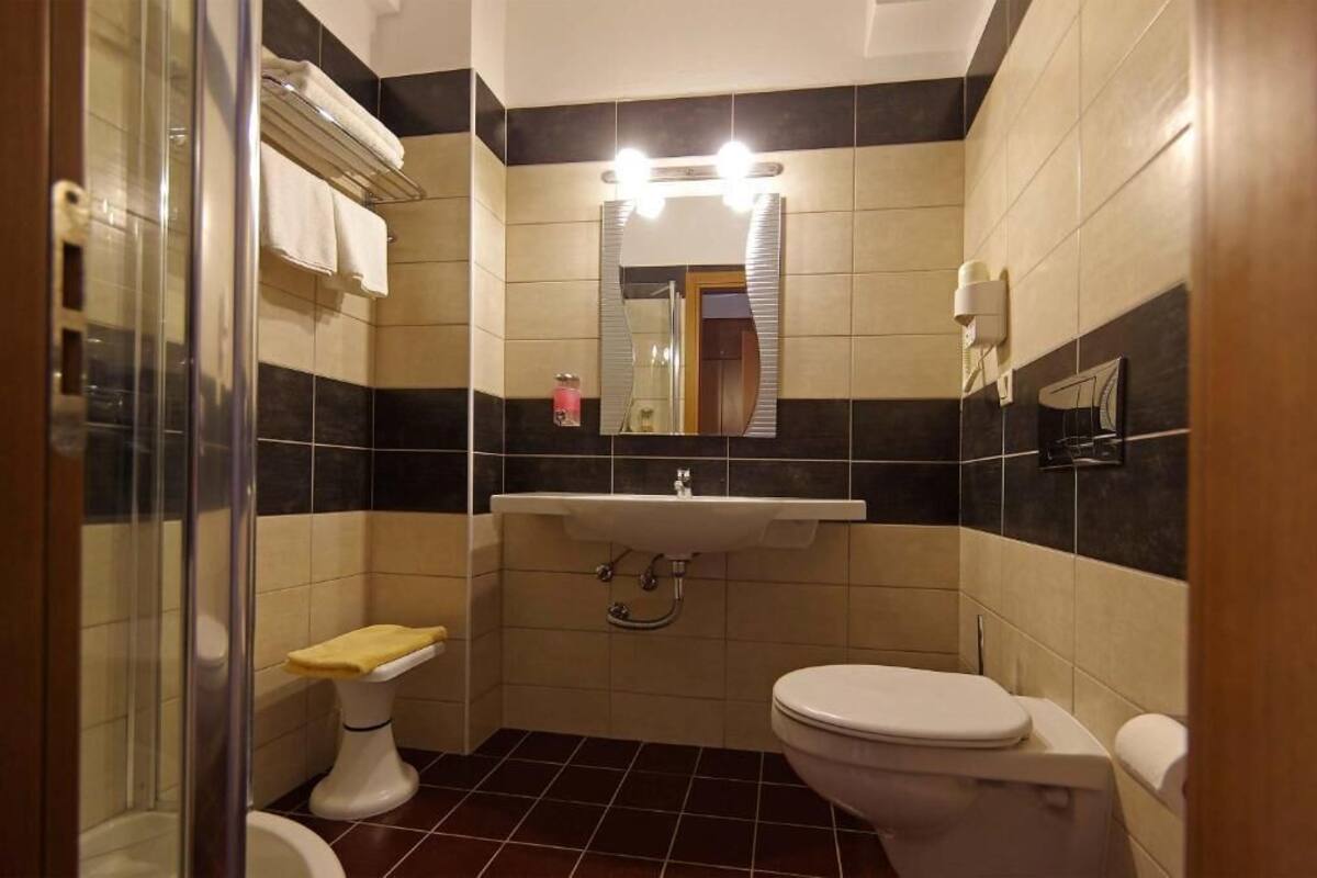 A bathroom with a glass shower enclosure, a white toilet, a sink with a mirror above it, and a towel rack.