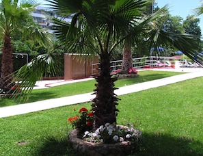 Un jardín cuidado con una palmera, una jardinera de piedra con flores y un camino despejado.