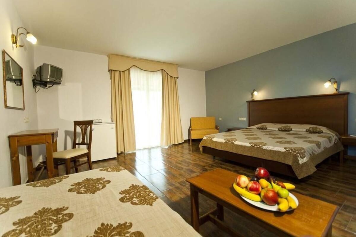 A hotel room with a bed, a desk, a chair, a television, and a fruit basket.