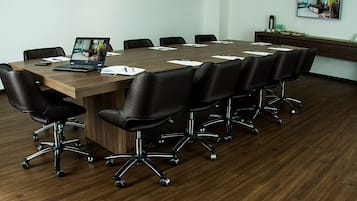 Un salón de conferencias con una larga mesa, sillas de cuero negro y una computadora portátil sobre la mesa.