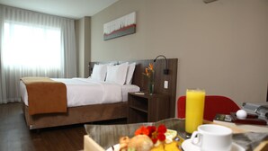 Una habitación de hotel con cama, mesita de noche y bandeja de desayuno con comida y una taza.