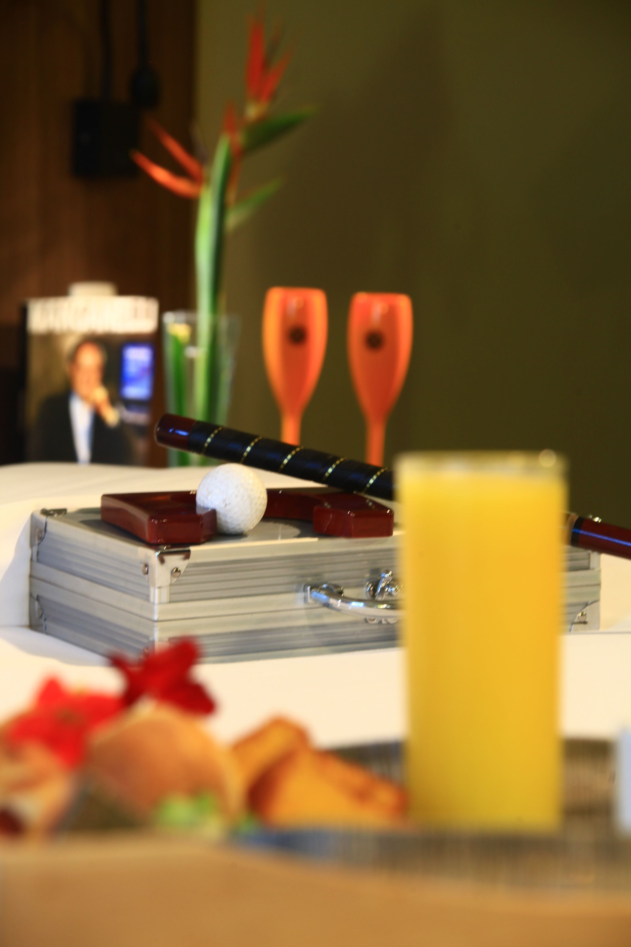 Una mesa con una pelota de golf, un palo de golf y un vaso de jugo de naranja.