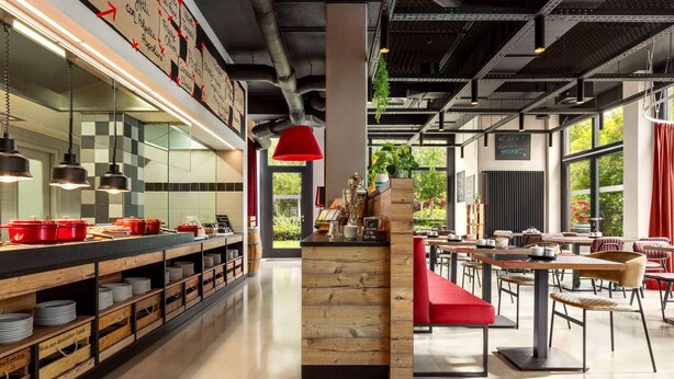 A modern restaurant interior with a long counter, red pendant lighting, and a view of the outdoors. - City Hotel MAX - Munich West (Munich)