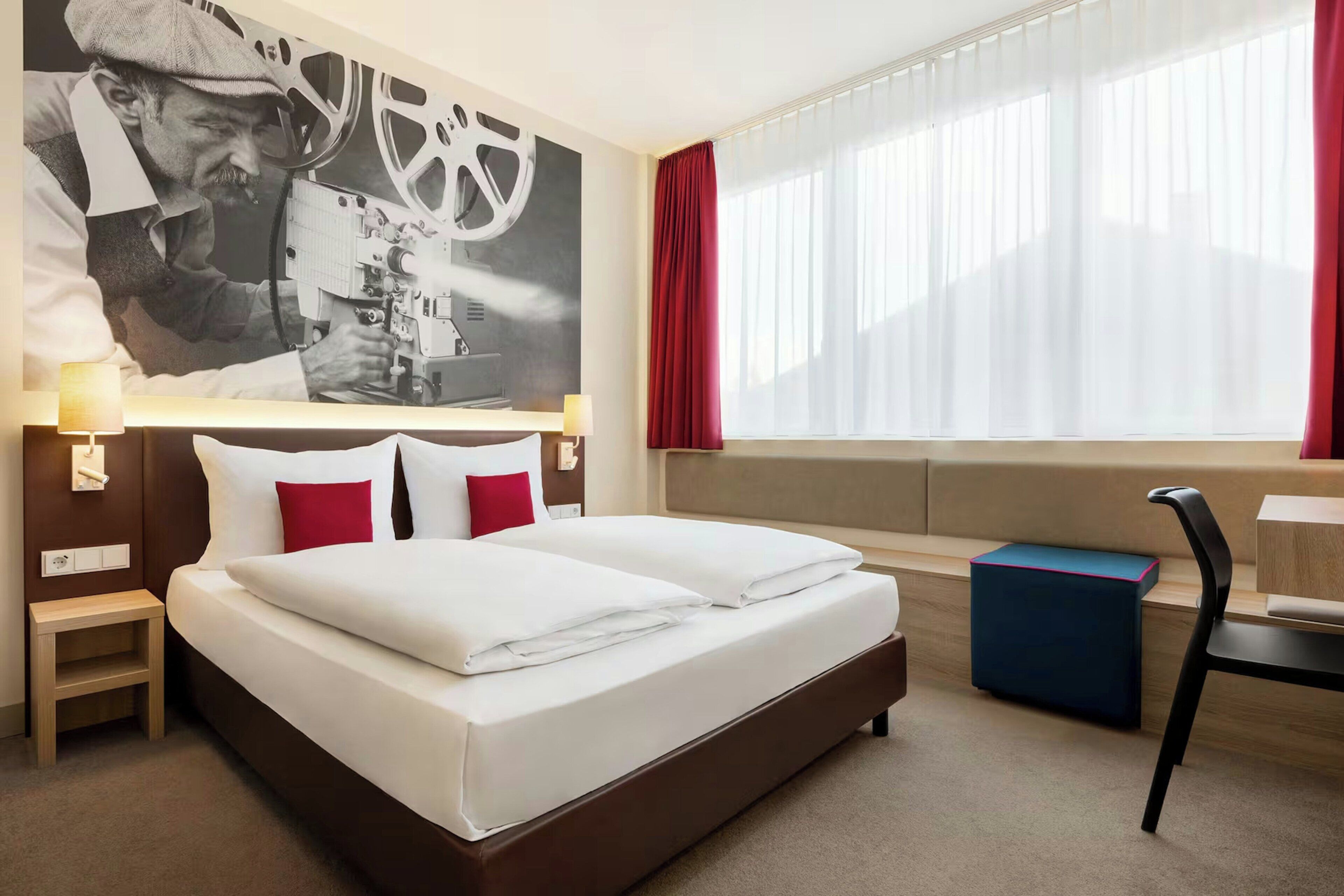 Une chambre d’hôtel avec un grand lit, un bureau, une chaise et une fenêtre avec des rideaux.