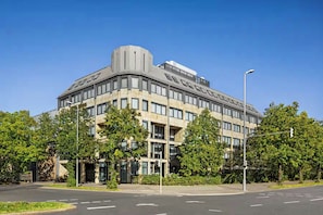 A modern building with a corner entrance, large windows, and a flat roof. - City Hotel MAX - Munich West (Munich)