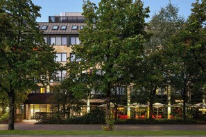Un hotel moderno con fachada de vidrio, zona de estar exterior y un jardín cuidado.