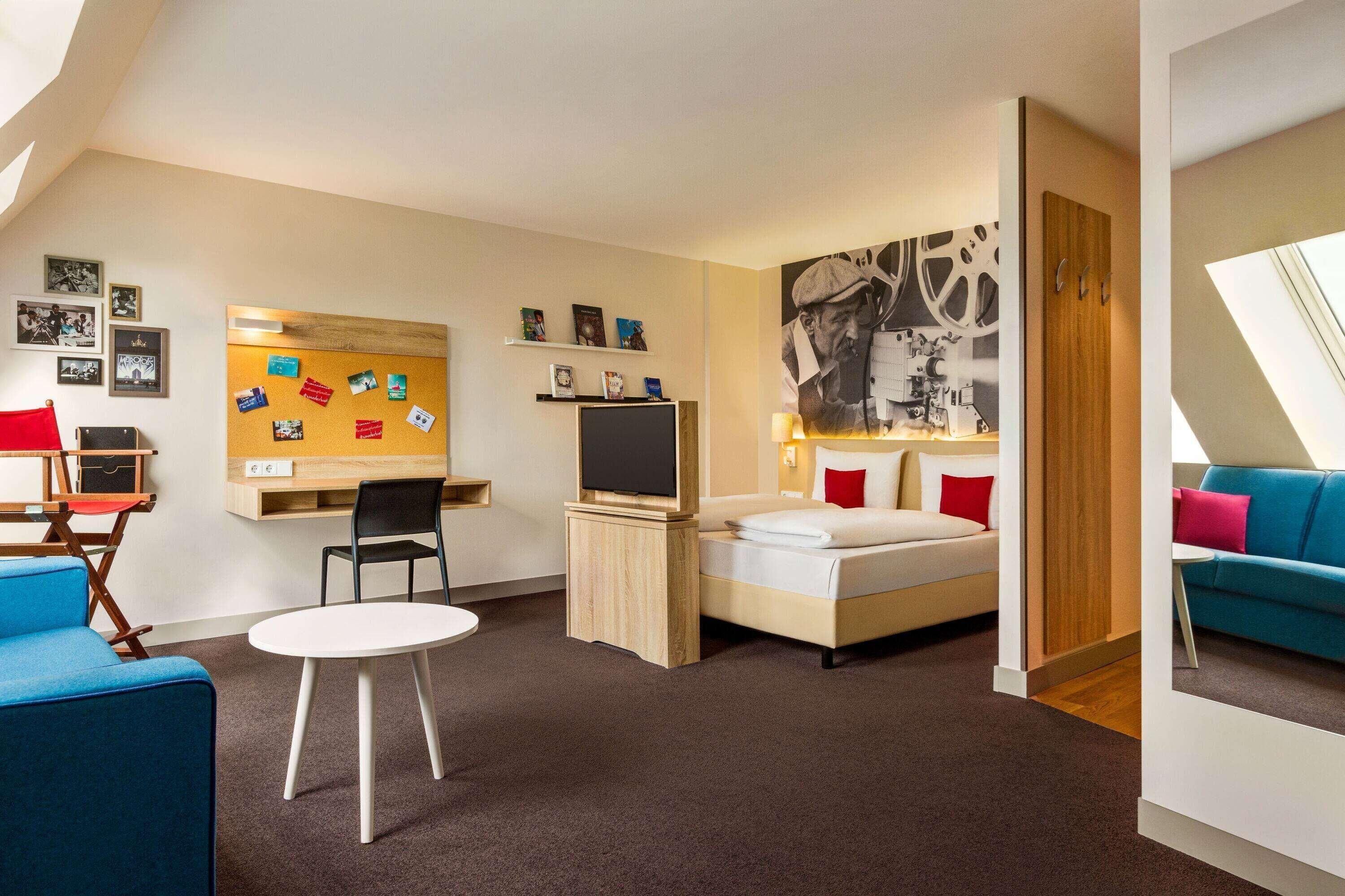Een moderne hotelkamer met een bed, een bureau met een televisie, een klein tafeltje, een blauwe stoel en een bank.