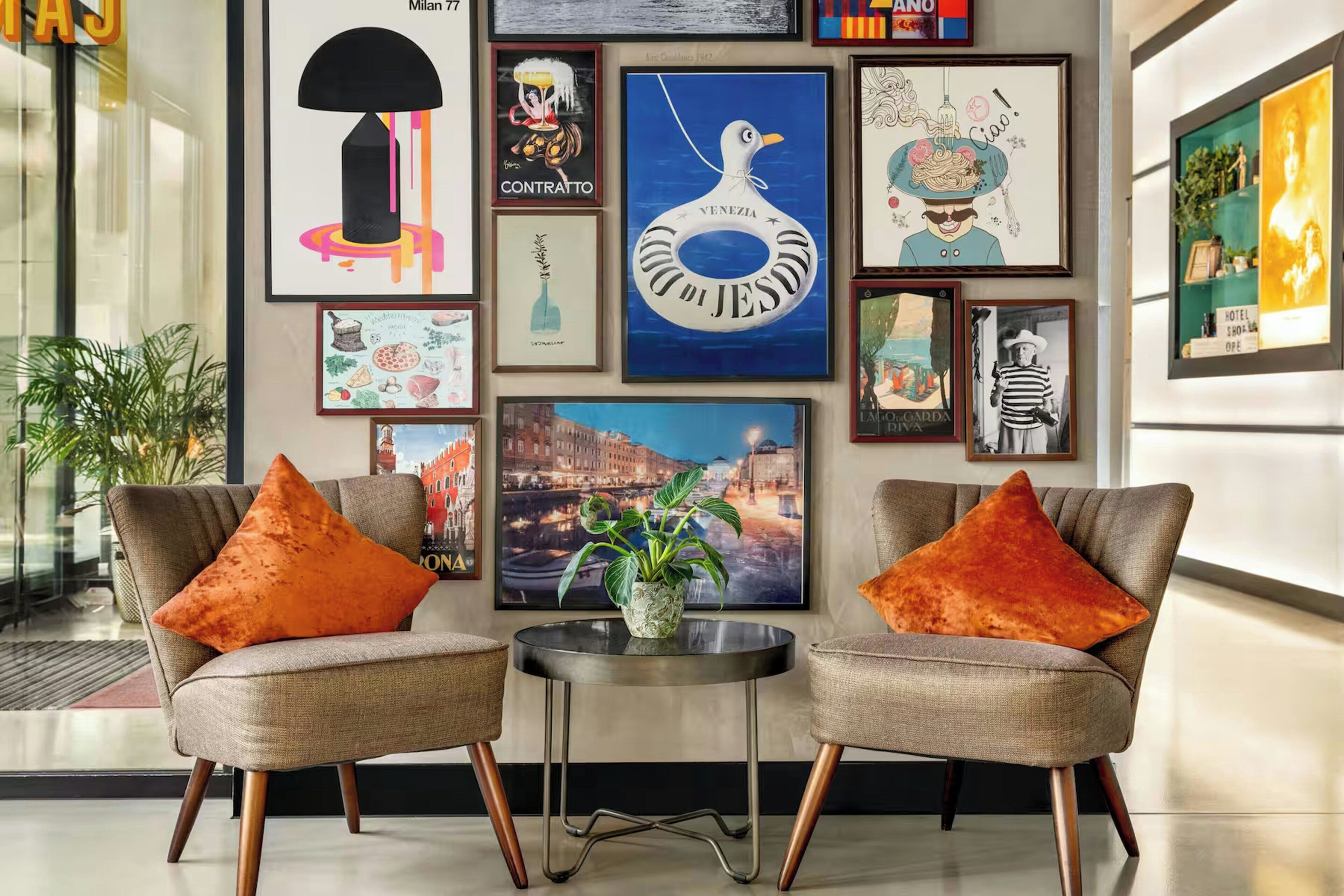 Ein modernes Interieur mit zwei Sesseln, einem kleinen Tisch und verschiedenen gerahmten Kunstwerken an der Wand.