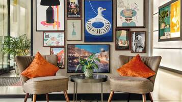 Ein modernes Interieur mit zwei Sesseln, einem kleinen Tisch und verschiedenen gerahmten Kunstwerken an der Wand.