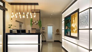 A modern reception desk with a lighted panel, a hanging light fixture, and a framed informational display on the wall. - City Hotel MAX - Munich West (Munich)