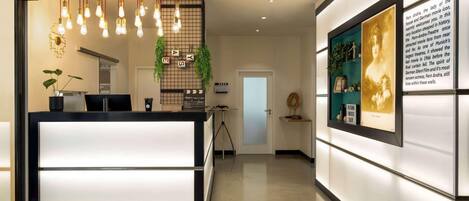 A modern reception desk with a lighted panel, a hanging light fixture, and a framed informational display on the wall.