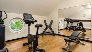 A gym with exercise equipment, a window, and a mirror. - City Hotel MAX - Munich West (Munich)