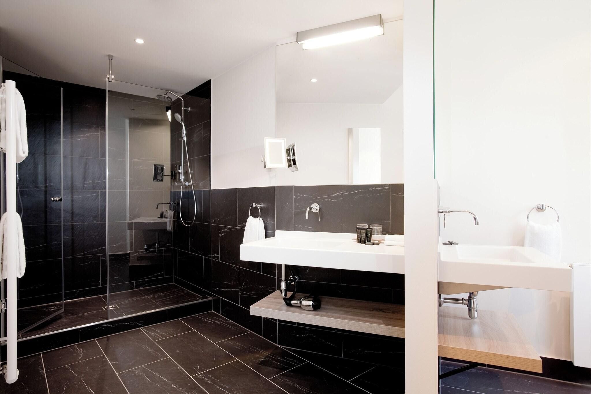 Ein modernes Badezimmer mit einer begehbaren Glasdusche, einem weißen Waschbecken und einem Spiegel darüber.