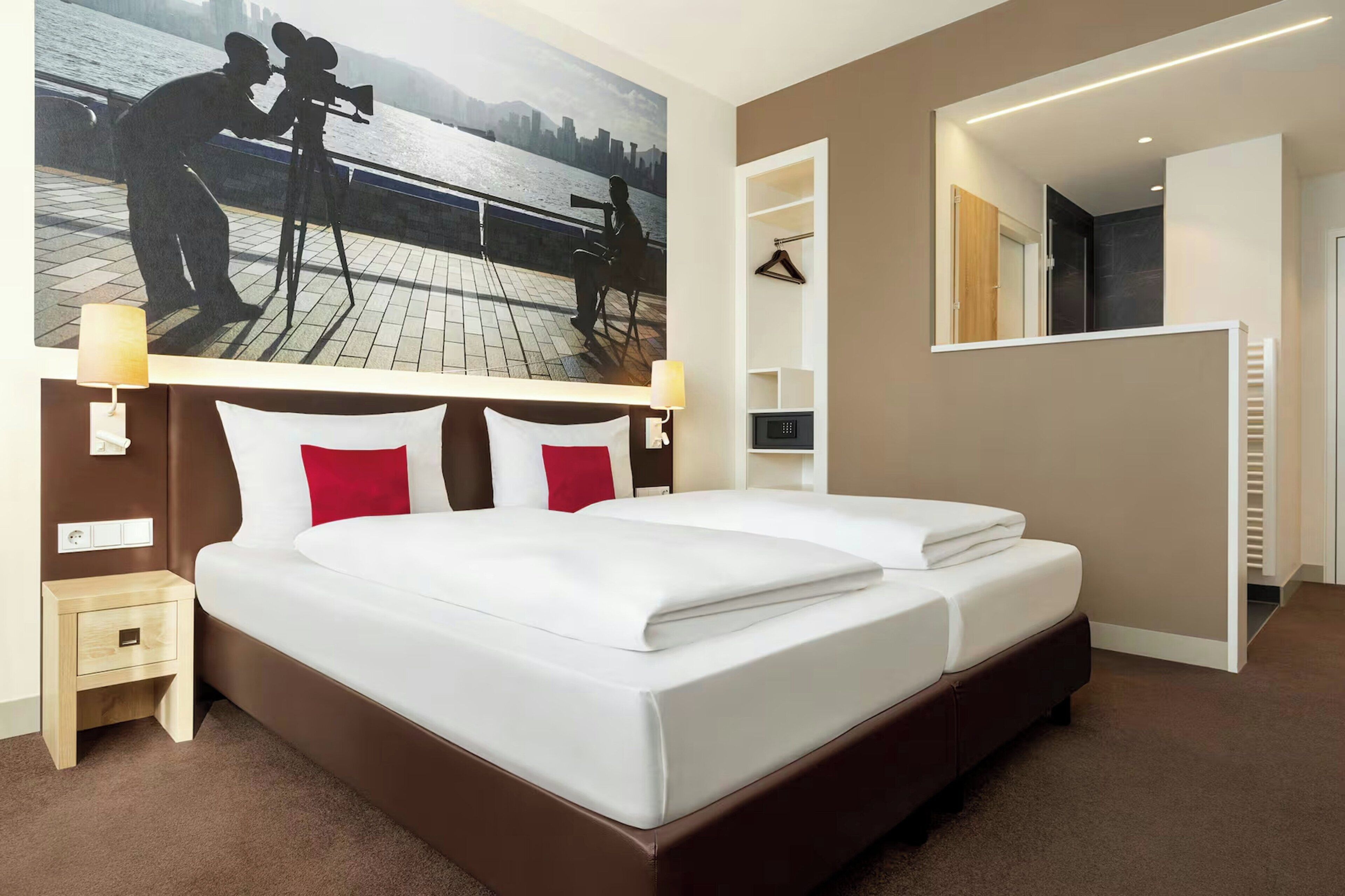 A hotel room with a large bed, a nightstand, a wall-mounted TV, and a mirror.