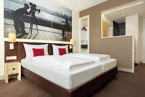 A hotel room with a large bed, a nightstand, a wall-mounted TV, and a mirror.