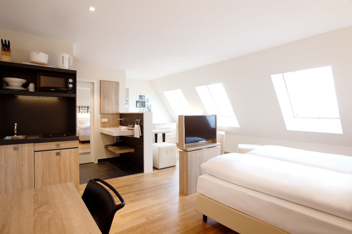 Una habitación de hotel moderna con cama, escritorio, televisor, kitchenette y tragaluces.