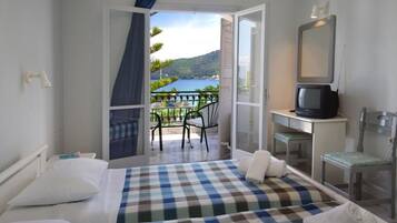 A hotel room with a bed, a desk with a computer, a chair, and a view of a balcony with a table and chairs.