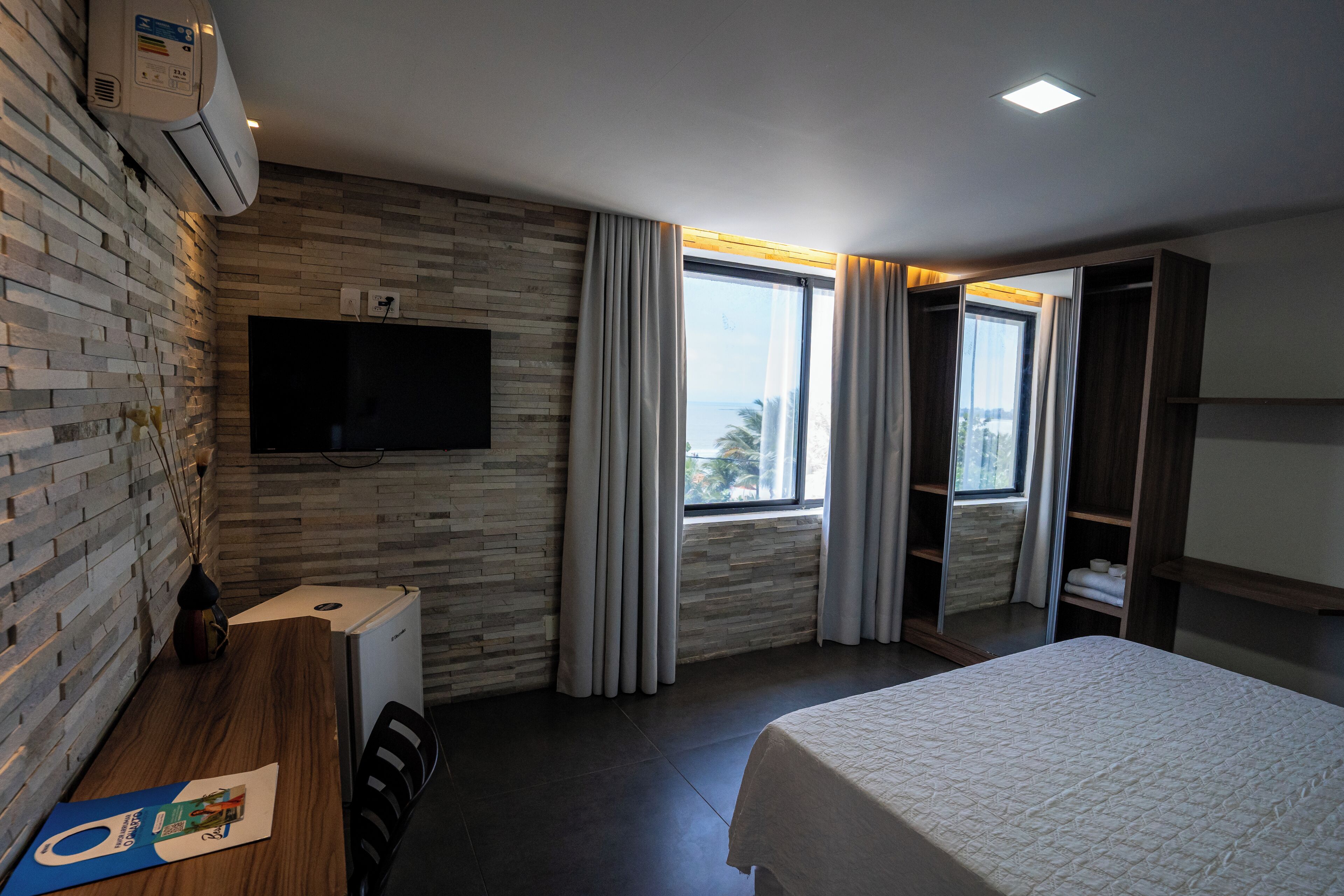 Une chambre d’hôtel moderne dotée d’un grand lit, d’un téléviseur à écran plat fixé au mur, d’un bureau avec une chaise et d’une fenêtre avec des rideaux.