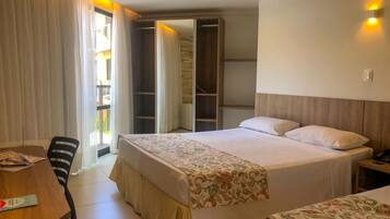 Ein Hotelzimmer mit einem großen Bett, einem kleineren Bett, einem Schreibtisch und einem Stuhl. Es gibt einen Kleiderschrank und einen Spiegel.