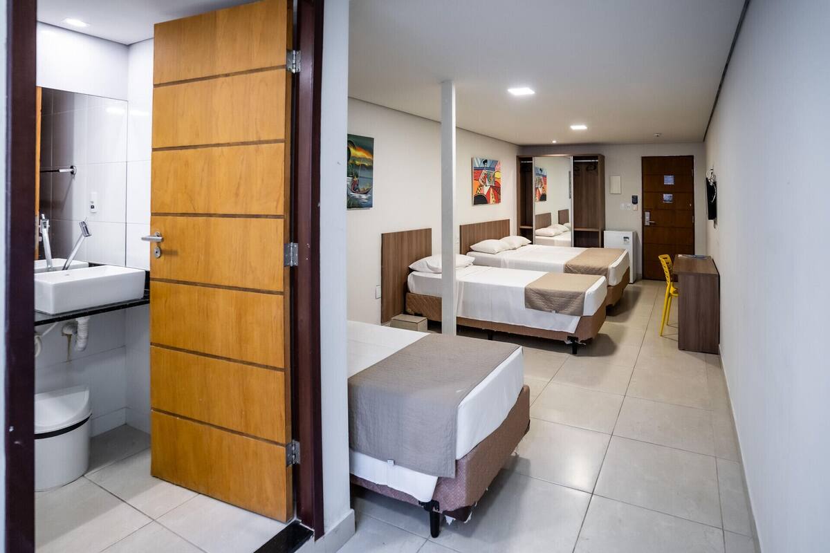 Una camera d'albergo con una porta in legno, un lavandino, due letti, una scrivania e una sedia.
