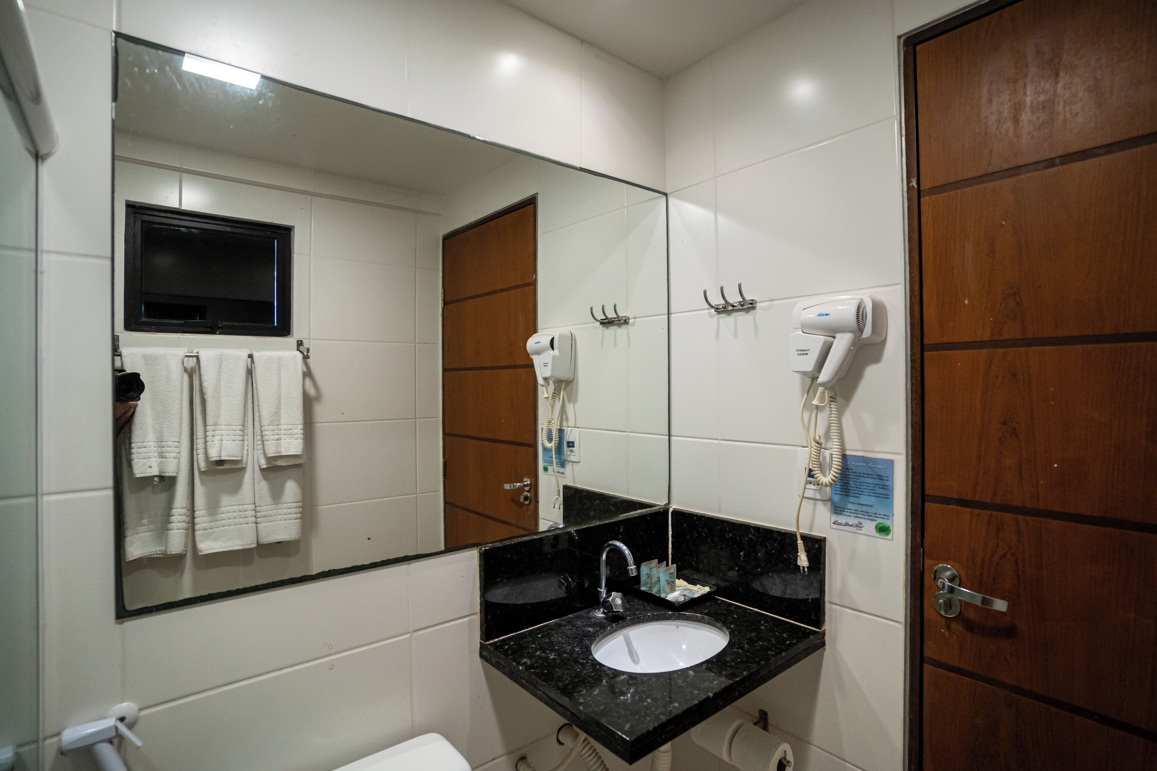 Un baño con un espejo grande, un lavabo, un perchero para toallas y un secador de pelo.