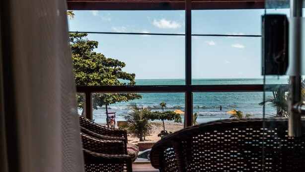 Vista desde una habitación con muebles de mimbre, con vista a una playa con sombrillas y palmeras.