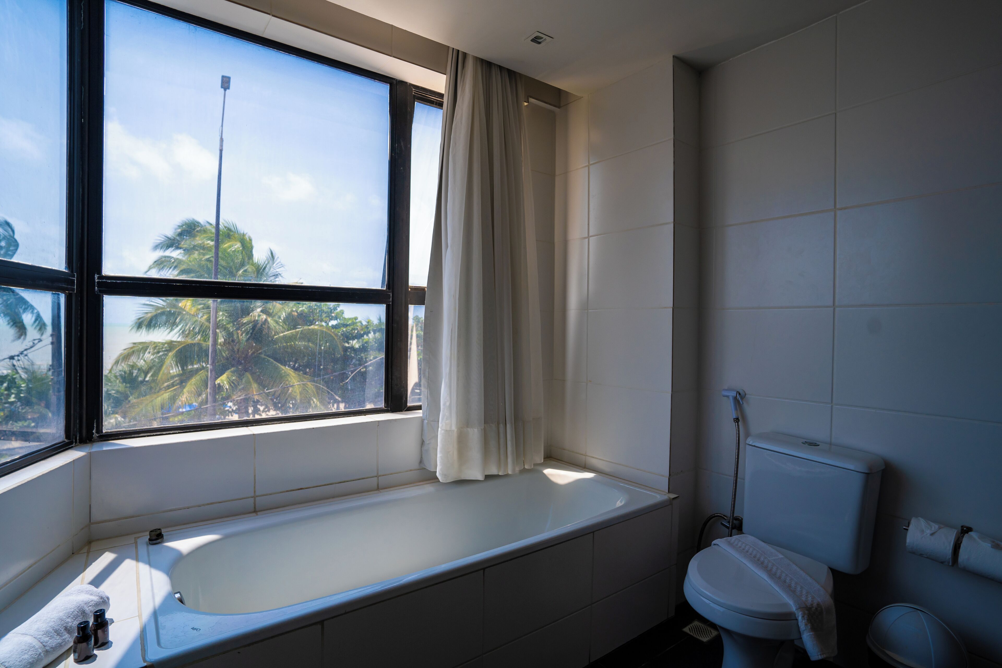 A bathroom with a bathtub, toilet, and window with curtains.