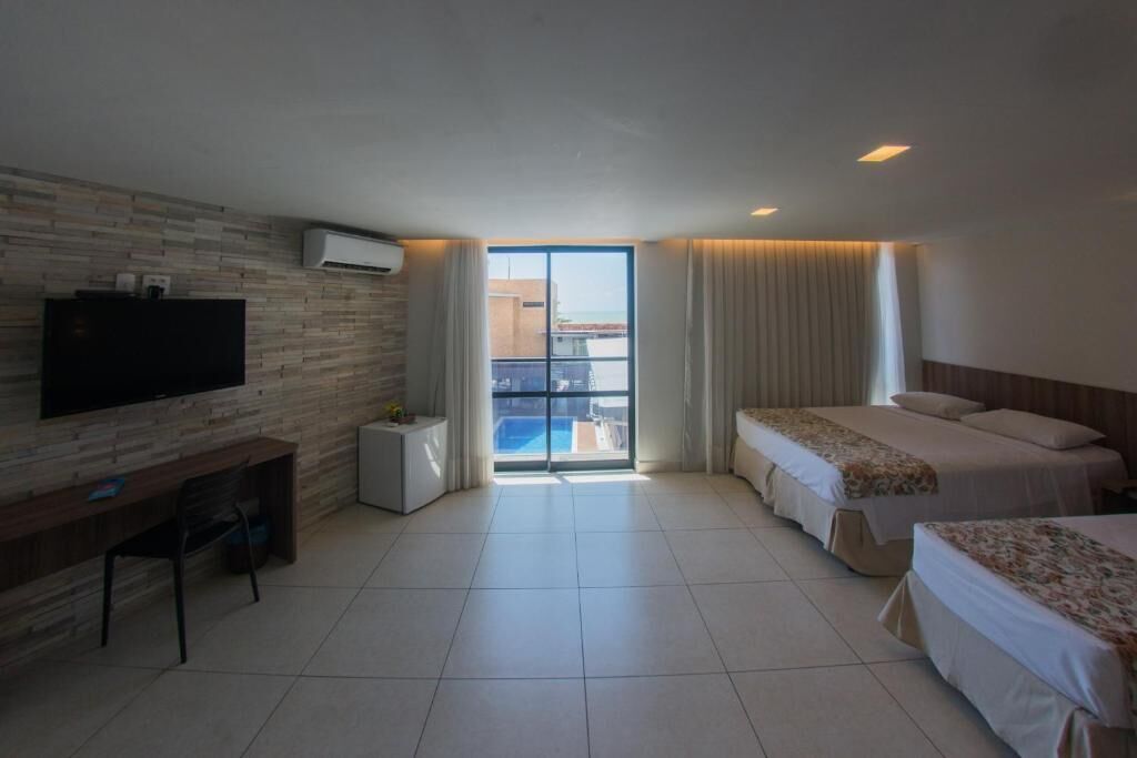 A hotel room with a TV, a desk, two beds, and a view of the pool.