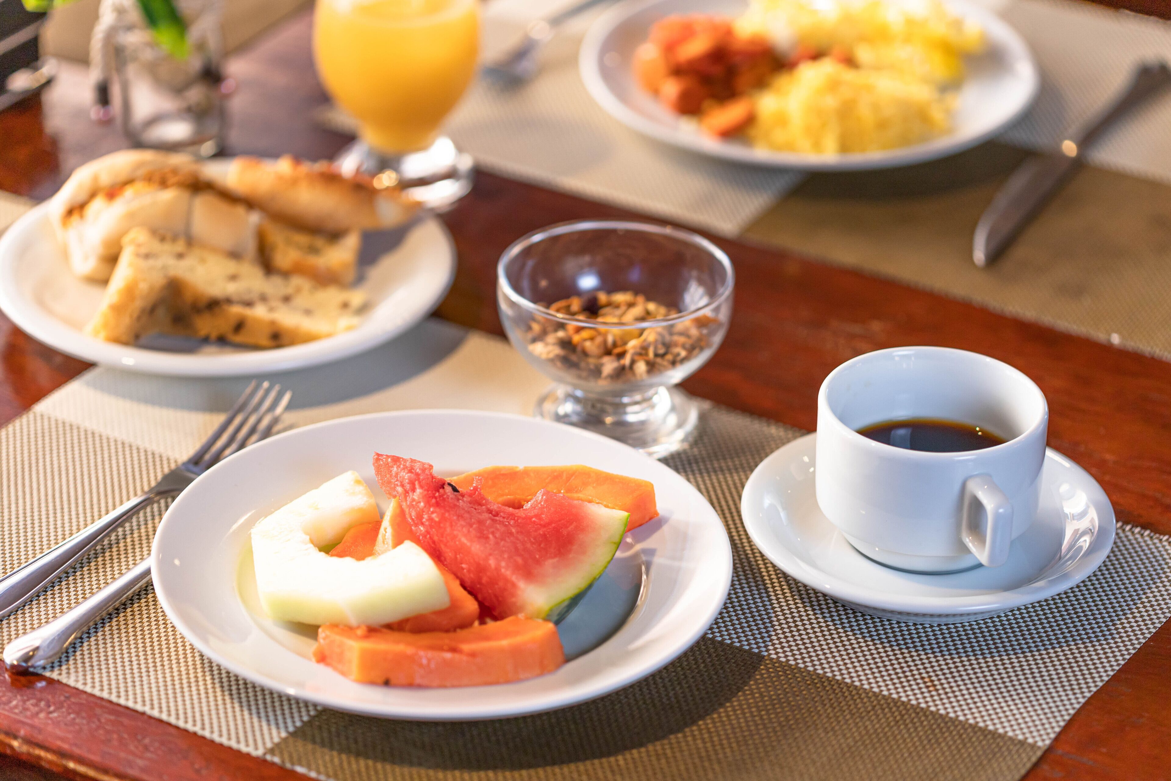 A breakfast setting with plates of food, a bowl of cereal, and a cup of coffee.