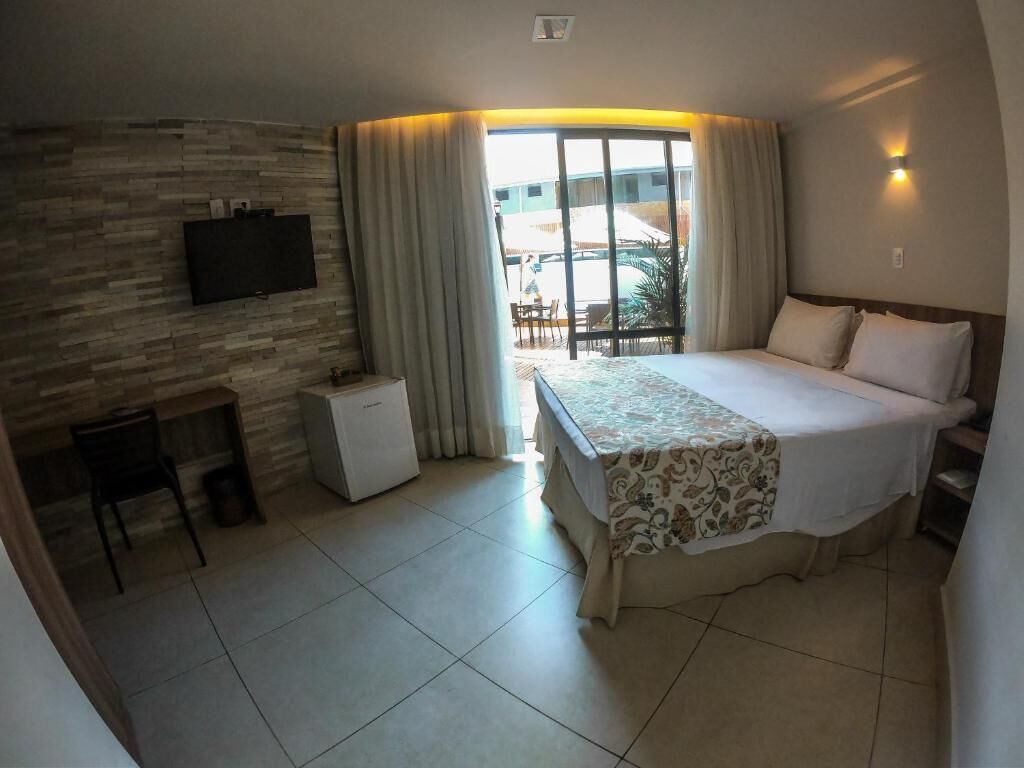 A hotel room with a bed, a desk, a television, and a view of the outdoors.