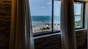 Una habitación con un amplio ventanal con vistas a una playa con sombrillas y gente.