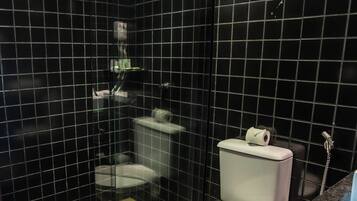 Un baño moderno con paredes de azulejos negros, suelo de madera, inodoro blanco y cabina de ducha con mampara de cristal.