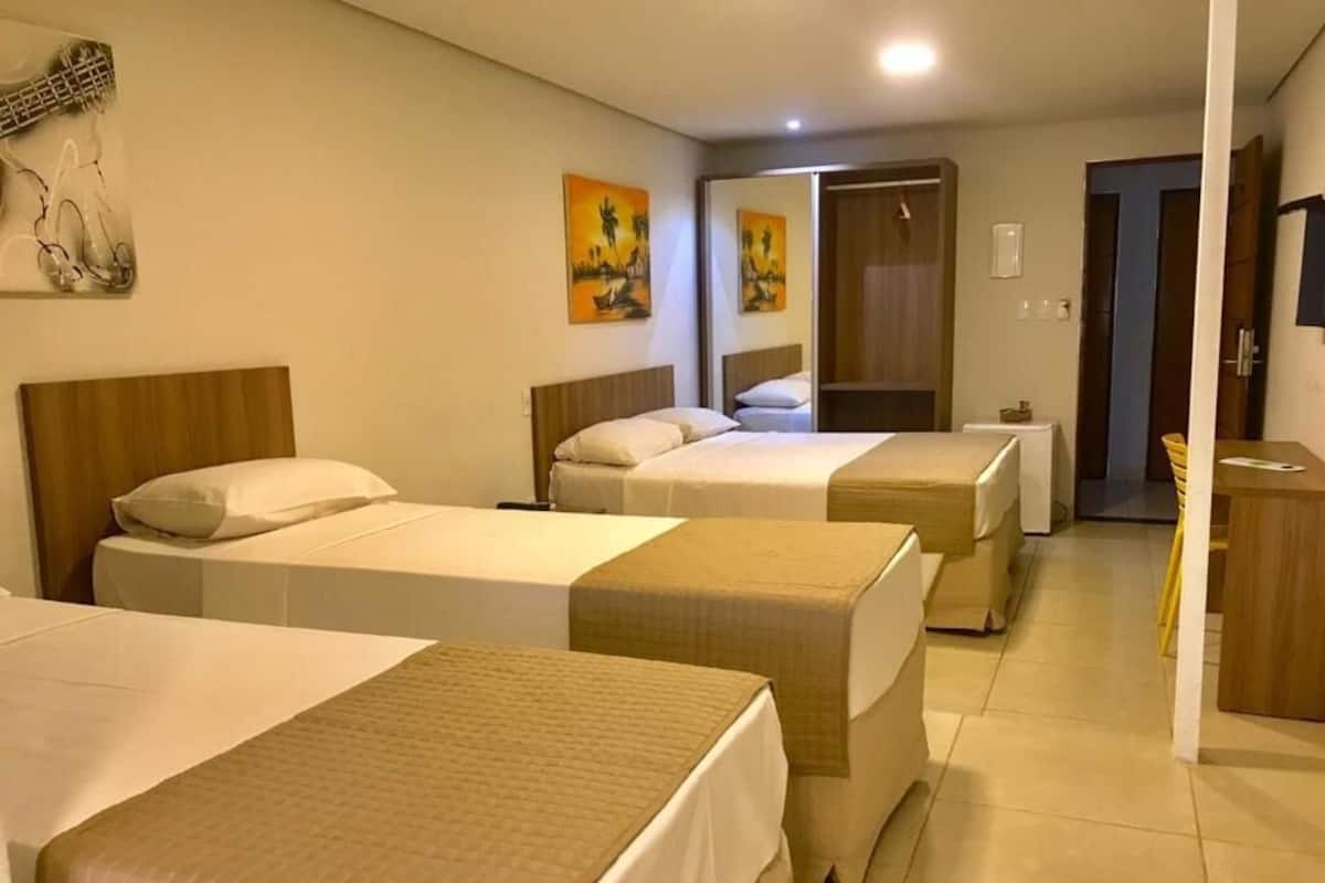 Camera d'albergo con tre letti, un armadio e uno specchio.
