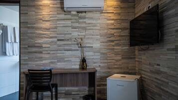 Ein modernes Badezimmer mit Steinwand, einem angebrachten Fernseher, einem kleinen Schreibtisch mit Stuhl und einem kompakten Kühlschrank.