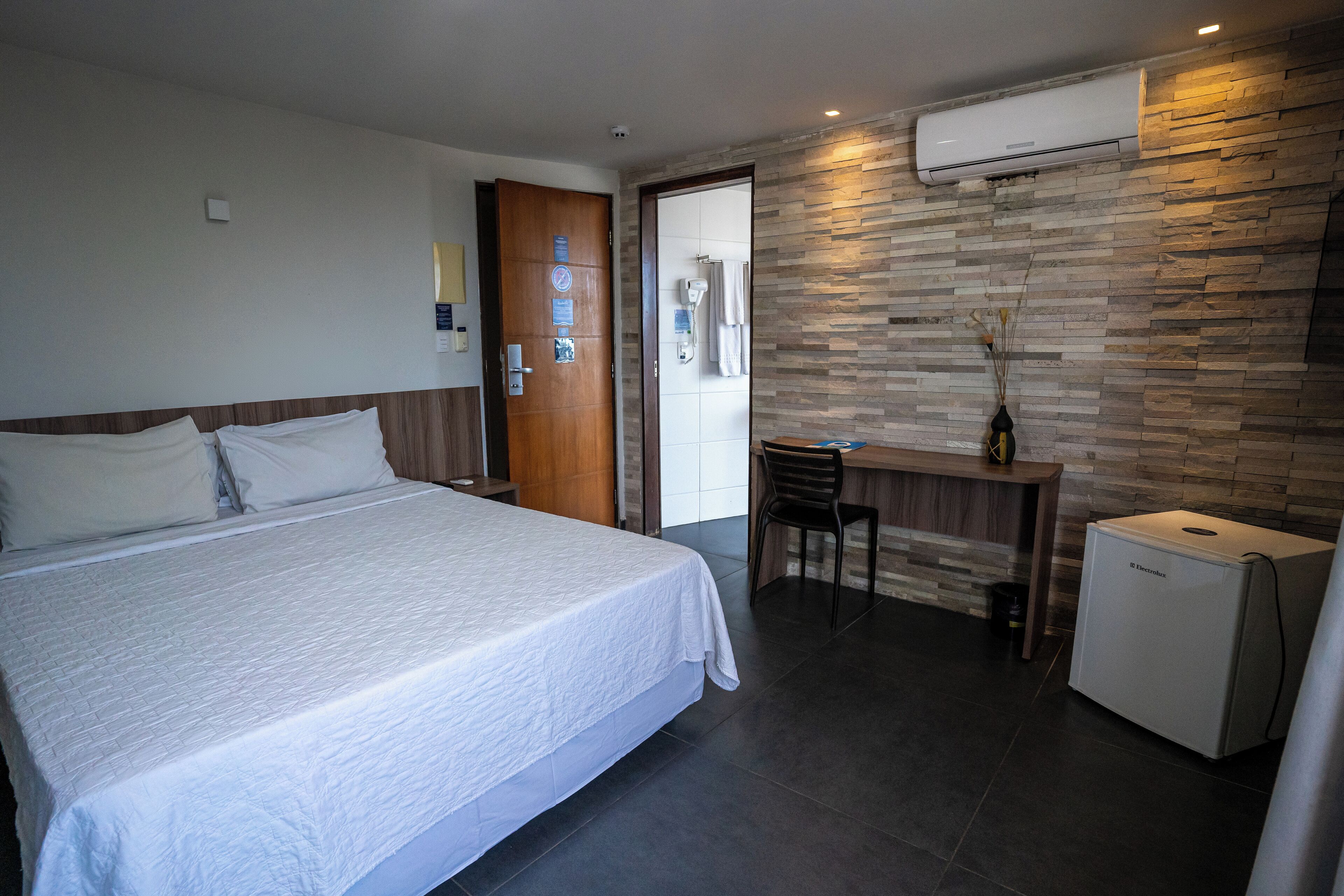 A hotel room with a bed, a desk, a chair, and a refrigerator.