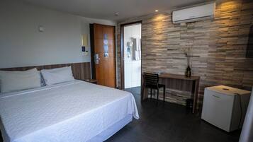 A hotel room with a bed, a desk, a chair, and a refrigerator.